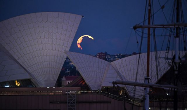 A pink supermoon obscured by clouds seen alongside the Sydney Opera House in Australia