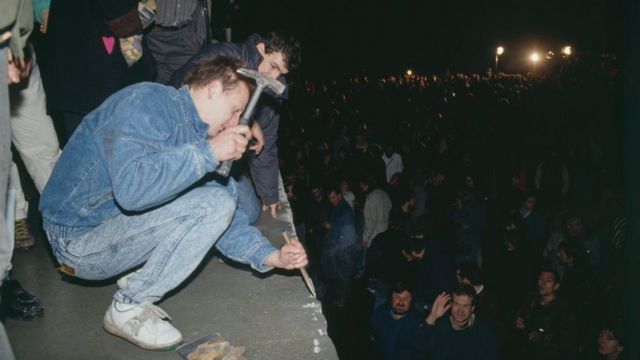 Un joven con un martillo sobre el Muro de Berlín.