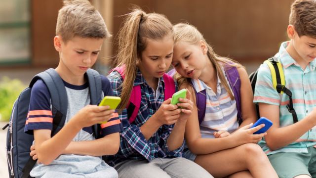 Niños sentados usando sus teléfonos celulares
