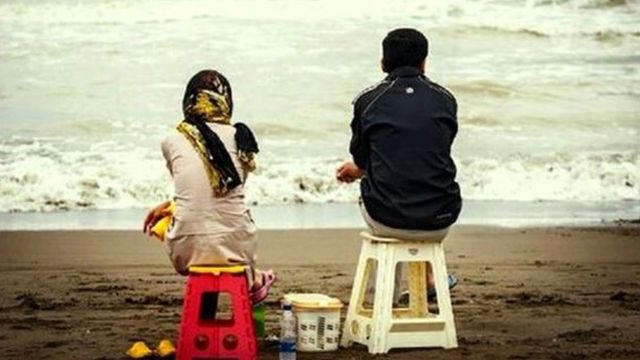 Couple sit on a beach in Iran
