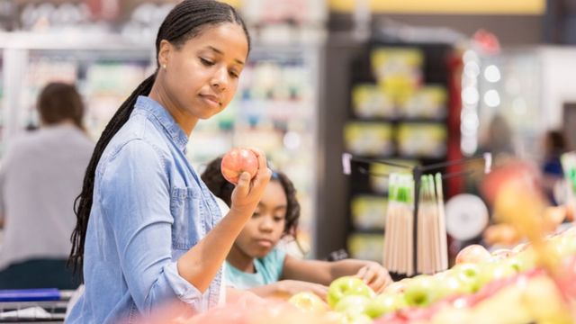 mulher e criança examinam frutas no supermercado
