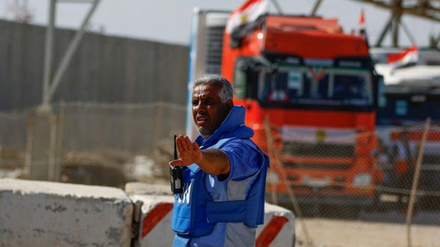 Un trabajador de la ONU hace un gesto mientras los camiones que transportan ayuda llegan al lado palestino de la frontera.