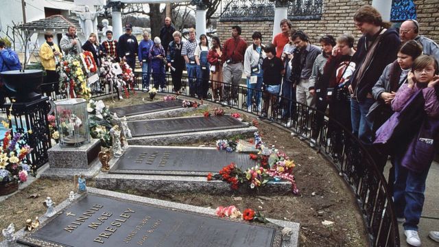 Fans se amontonan alrededor de la pequeña reja que los distancia de la tumba de Elvis, en el centro, rodeada de las de sus familaires.