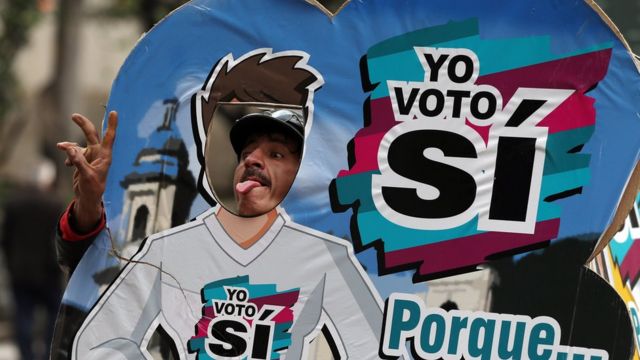 Homem posa para foto ao lado de cartaz do "sim" em Bogotá, na Colômbia