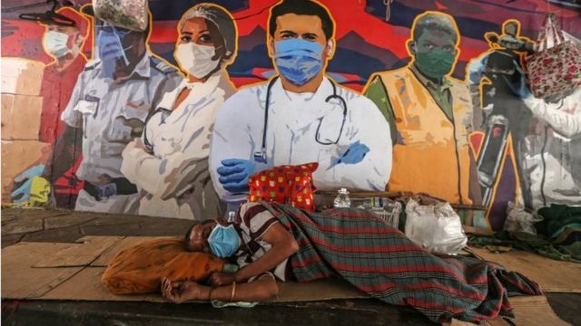 A man wearing face mask sleeps in front of the wall showing a graffiti honoring frontline workers in the fight against the spread of coronavirus COVID-19, in Mumbai, India, 22 March 2021.