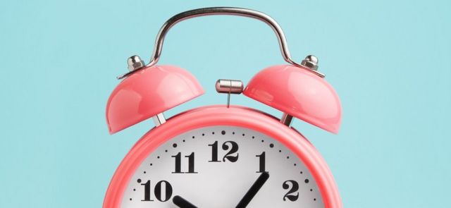 Pink alarm clock on turquoise-blue background