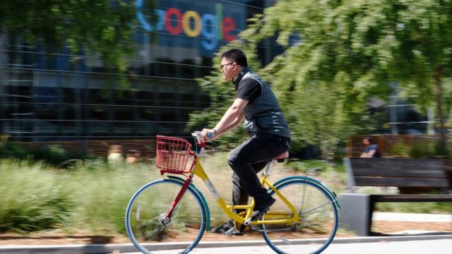 Homem pedalando na frente da sede do Google