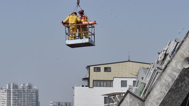 A man is lifted by a crane out of the rubble by rescue workers