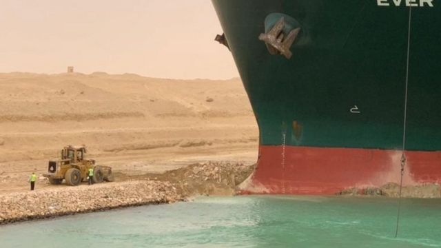 Des ouvriers sont vus à côté d'un porte-conteneurs qui a été frappé par un vent violent et s'est échoué dans le canal de Suez, en Égypte, le 24 mars 2021.