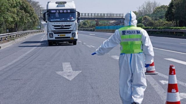 Policial paramentado com roupas anticovid faz sinal para um caminhão em uma estrada parar