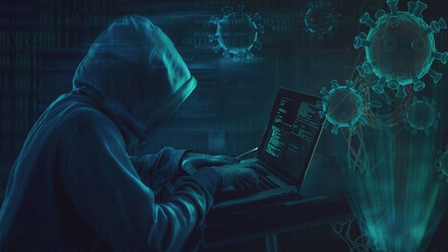 Un hombre con una capucha escribe en su computadora, en medi de imágenes de coronavirus