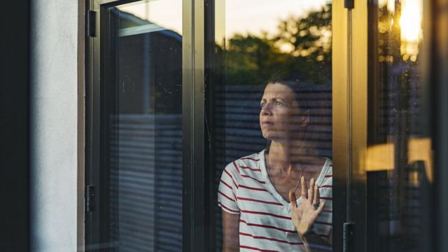 Mujer mira al horizonte a través de una ventana.