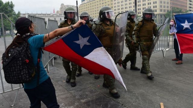 Manifestantes con banderas chilenas frente a los policías chilenos.