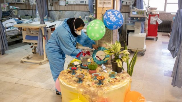An Iranian medical personnel wearing a protective suit places a mirror on a Haft-Seen (Seven-S) table, The historical symbol for the Iranian New Year, in a COVID-19 ward in Firoozabadi hospital in Shahr-e-Rey neighborhood in the south of Tehran on the day of Nowruz