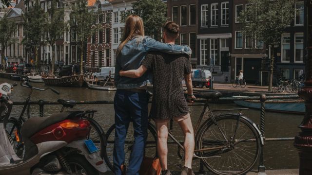 Une grande femme enlace un homme devant un canal à Amsterdam.