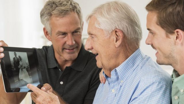 Fotografia de homens brancos mostrando uma fotografia para um idoso branco