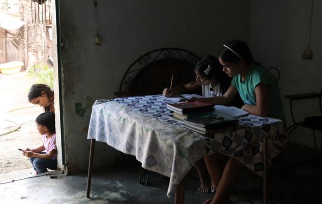 Valeria Torres with one of her students working at the table. Through the open door you can see the dirt courtyard and two younger children waiting.