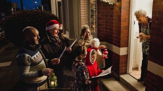 Группа поет рождественские песни у двери дома