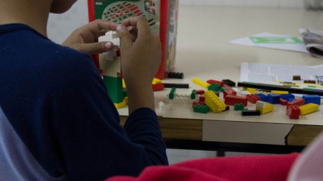 Criança de costas brinca com peças encaixáveis de Lego