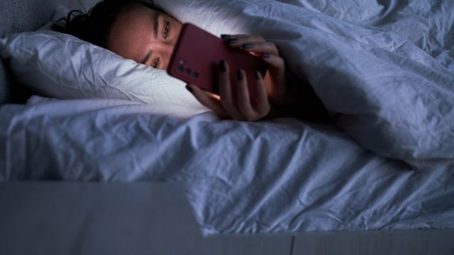 woman looks at cell phone lying on bed