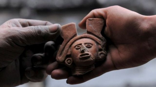 Aztek sunağında bulunan kilden yapılmış insan figürlerinden biri, bir arkeolog tarafından gösteriliyor