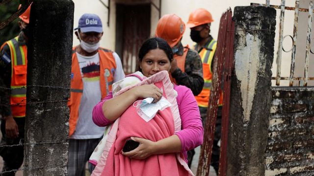 Una mujer con un bebé en brazos desaloja su casa en Honduras acompañada del ejército