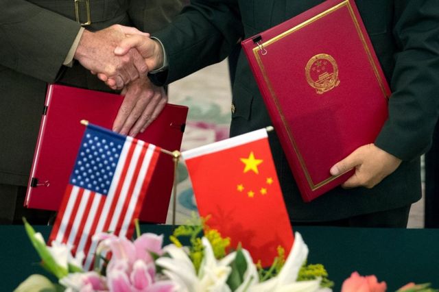 Close up of US and Chinese official shaking hands, holding documents. Flags of both countries in the foreground