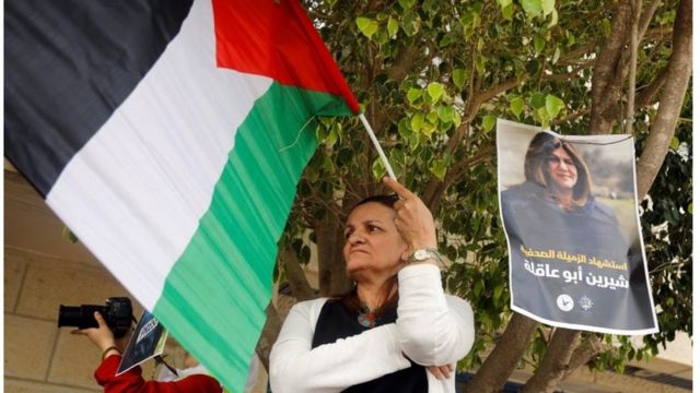 A woman raises the Palestinian flag next to a photograph of Shireen Abu Akleh.