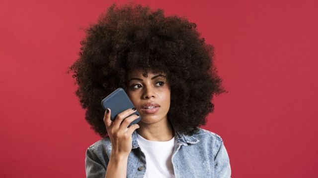 Una mujer sostiene un teléfono aparentemente escuchando un mensaje de audio.