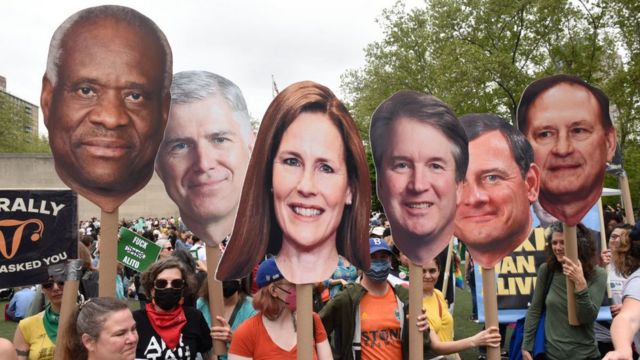Protesters hold photos of six Supreme Court justices