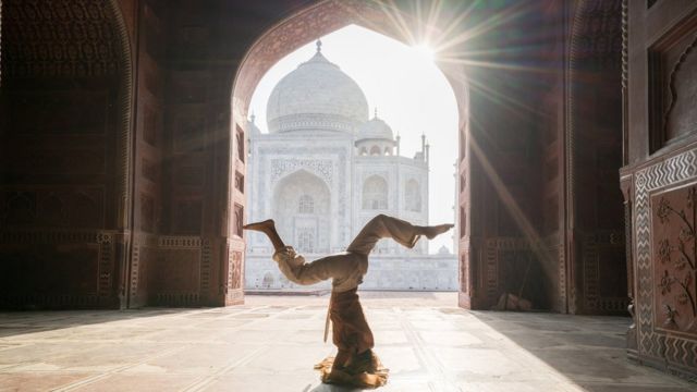 Mulher faz posição de ioga de cabeça pra baixo dentro de templo histórico na Índia