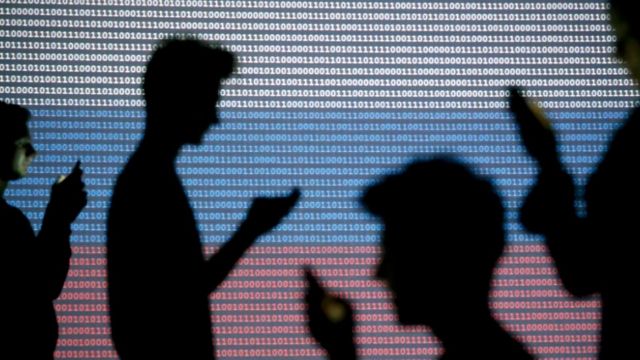 Sombras de personas revisando sus teléfonos celulares contra un fondo hecho con códigos binarios y los colores de la bandera rusa.