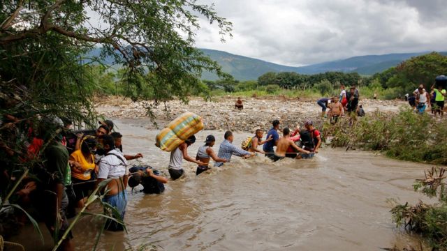 Personas pasando a y cargadas con bultos de distintos tamaños la frontera entre Venezuela y Colombia.
