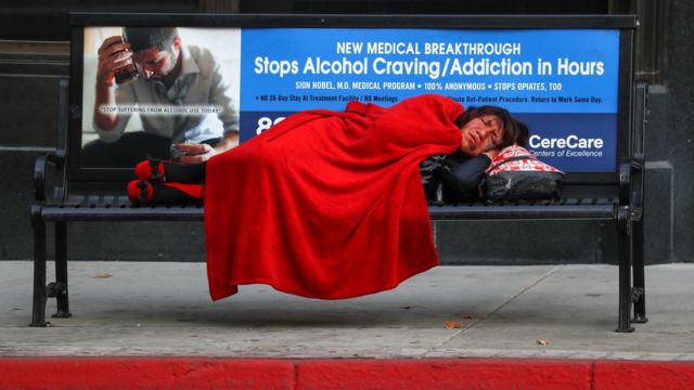 Moradora de rua dormindo em banco em uma rua de Los Ângeles