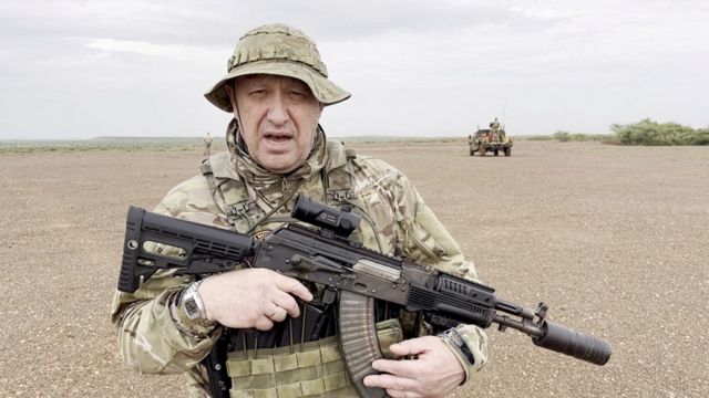 Prigozhin segurando grande arma e falando em área árida