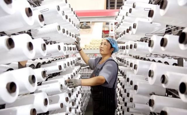 Mulher trabalhando com dezenas de linhas tecendo na China