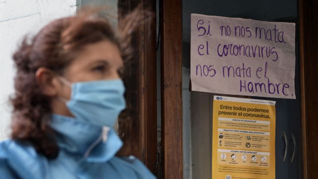 Una mujer en Buenos Aires usando un tapabocas frente a un cartel que dice: "Si no nos mata el coronavirus, nos mata el hambre".
