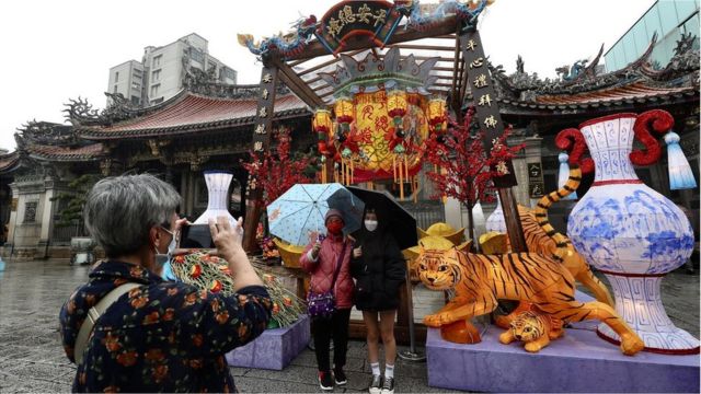 People wearing masks take a photo outside the Longshan Temple during the celebration of the Lunar New year in Taipei, Taiwan, 01 February 2022. The Lunar New Year, also known as Spring Festival in China, falls on 01 February in 2022, marking the beginning of the Year of the Tiger. Mass public gathering are suspended and crowd controls are being implemented in temples as preventive measures against the spread of COVID-19.