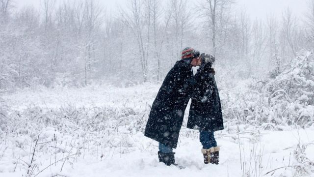 Dos personas se besan en un bosque mientras cae la nieve