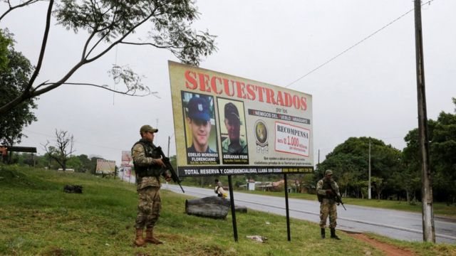 Soldados patrullan frente a un cartel de secuestro.