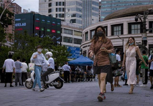 在上海街头，行人走在显示最新经济和证券交易所子信息的大屏幕前。(photo:BBC)