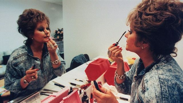 Tammy Faye Bakker passando maquiagem em frente ao espelho no camarim do programa