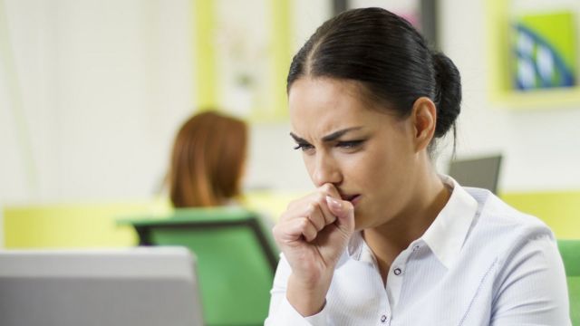 Mujer tose frente a la computadora.