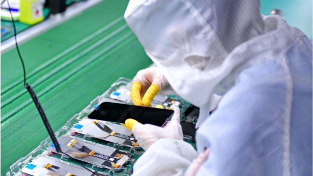Un empleado trabaja en la línea de producción de pantallas para teléfonos inteligentes 5G en una fábrica.