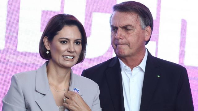 Bolsonaro olhando com feição fechada para Michelle, que sorri, em evento 