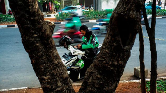 Seorang pengemudi ojek menunggu di pinggir jalan di Jakarta.