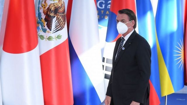 Bolsonaro caminha de máscara diante de bandeiras de outros países