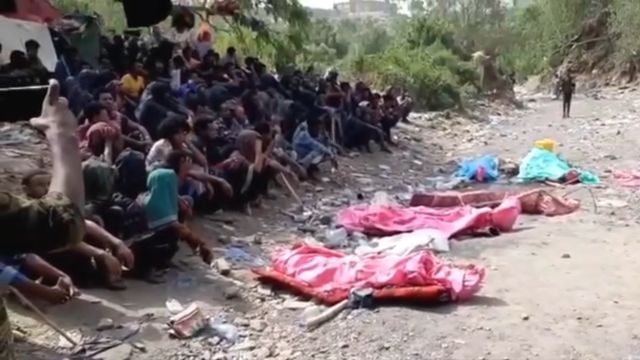 Migrantes miran cuerpos cubiertos durante un entierro en la frontera entre Arabia Saudita y Yemen