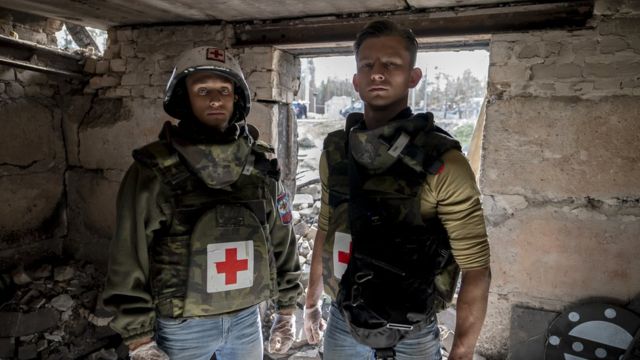 Fotografia colorida mostra dois homens brancos com uniformes militares em um edifício destruído