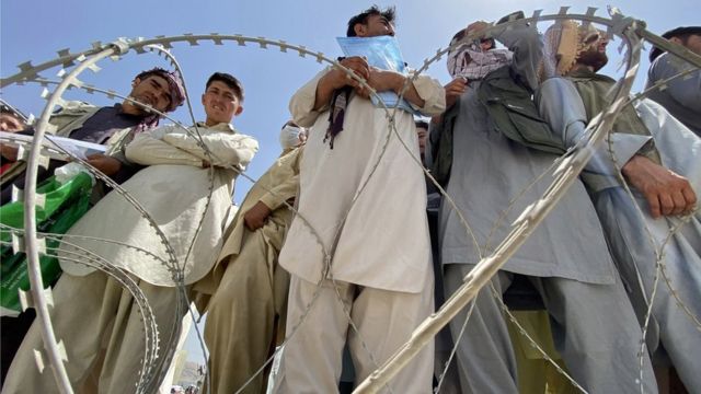 أفغان يقفون وراء أسلاك شائكة في المطار.